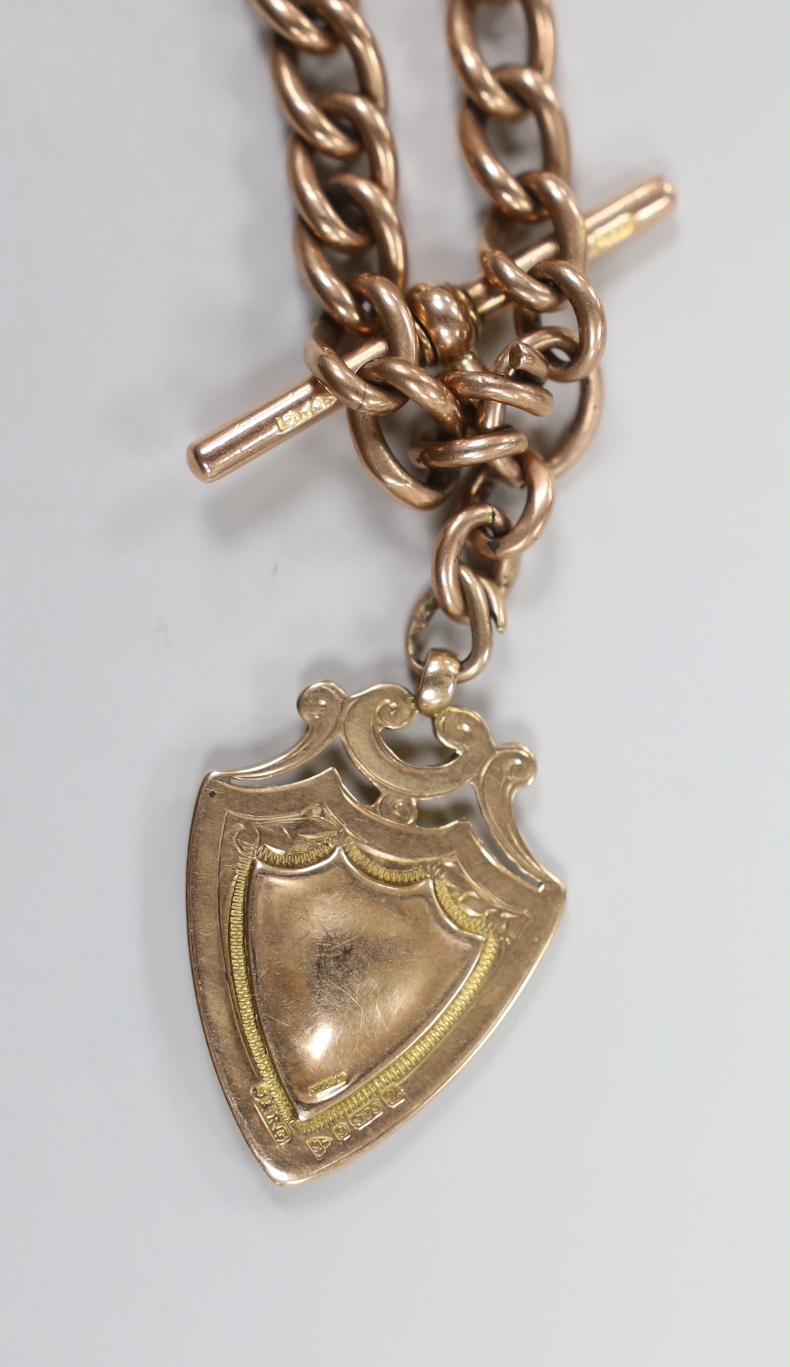 An early 20th century 9ct rose gold albert, 36cm, hung with a 9ct gold shield shaped medallion, 52.3 grams.